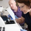 A man and a woman researcher analyze results over a white microscope.